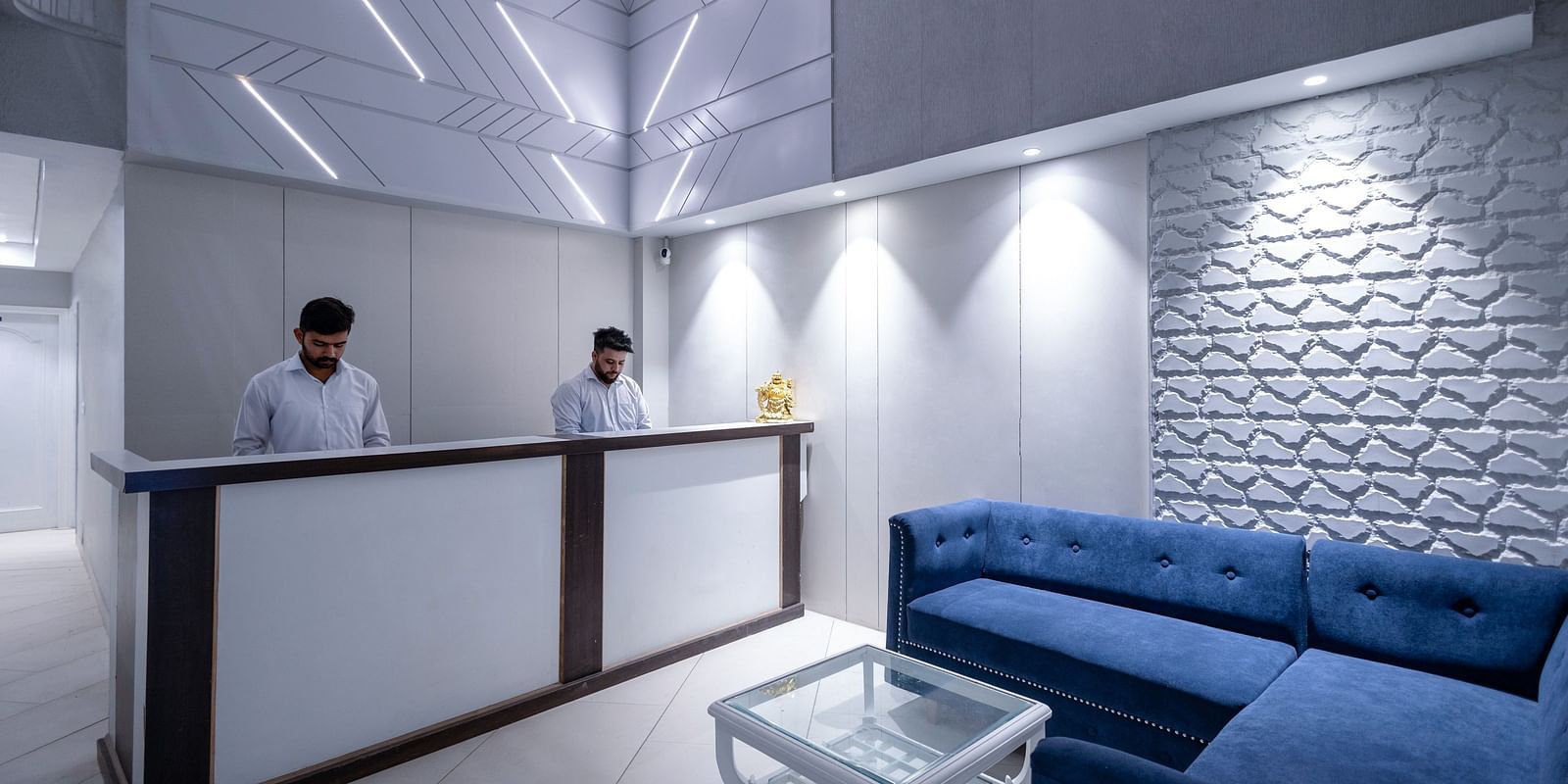 the reception area with two staff members dressed in white formal shirts standing behind the reception desk - Hotel Downtown17, Chandigarh