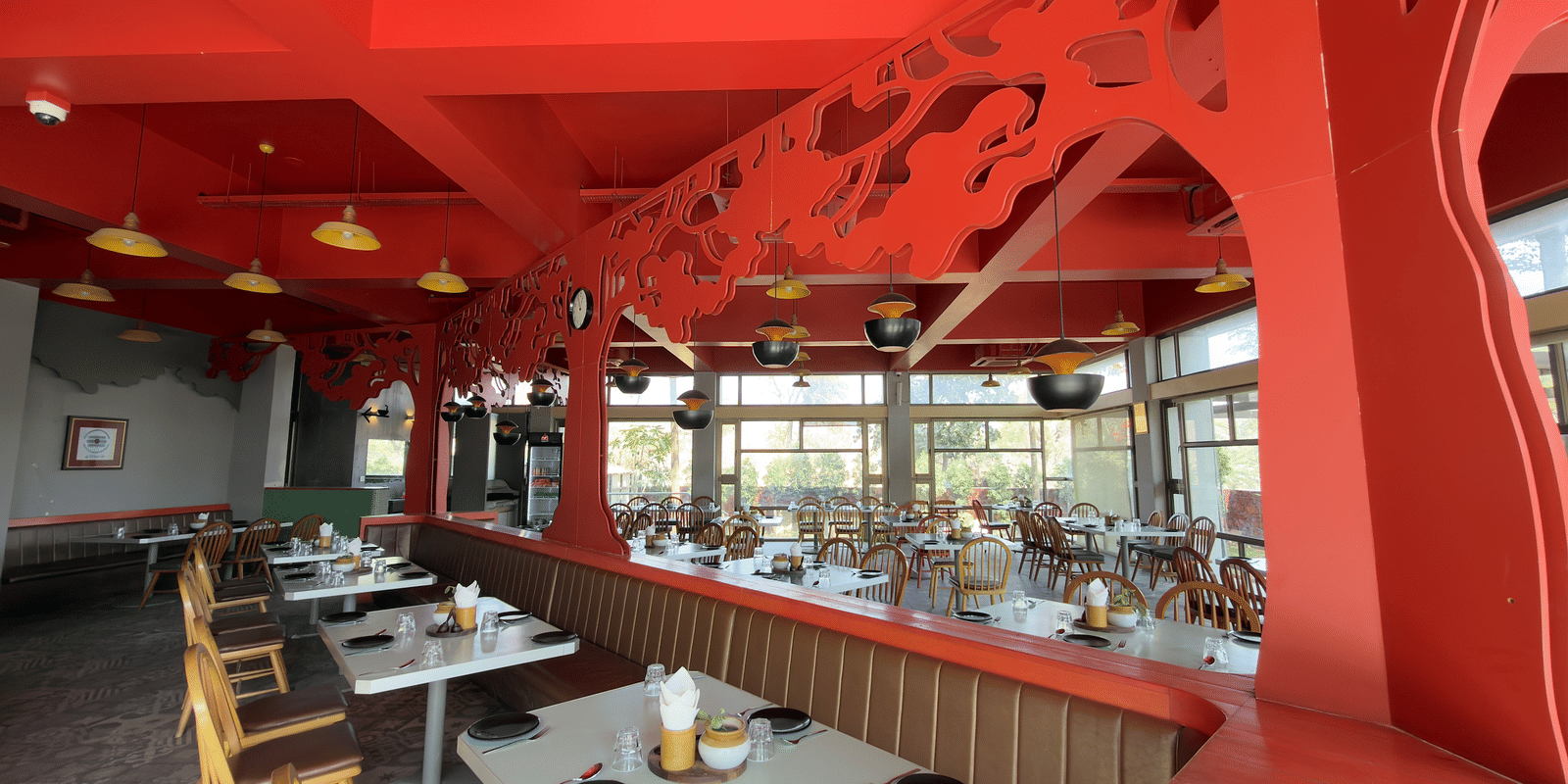 The restaurant at Vinti Resort, Ambaji, lit for meals, features a striking pink ceiling and comfortable tables set for dining.