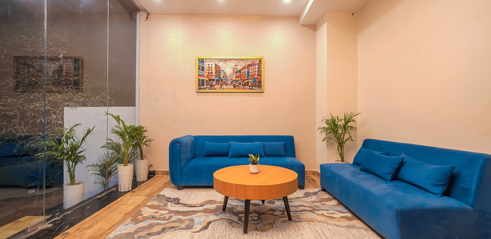 A lounge area at Perfectstayz Premium Varanasi, featuring 2 blue sofa, an artistic wall frame, a round table, and a rug.