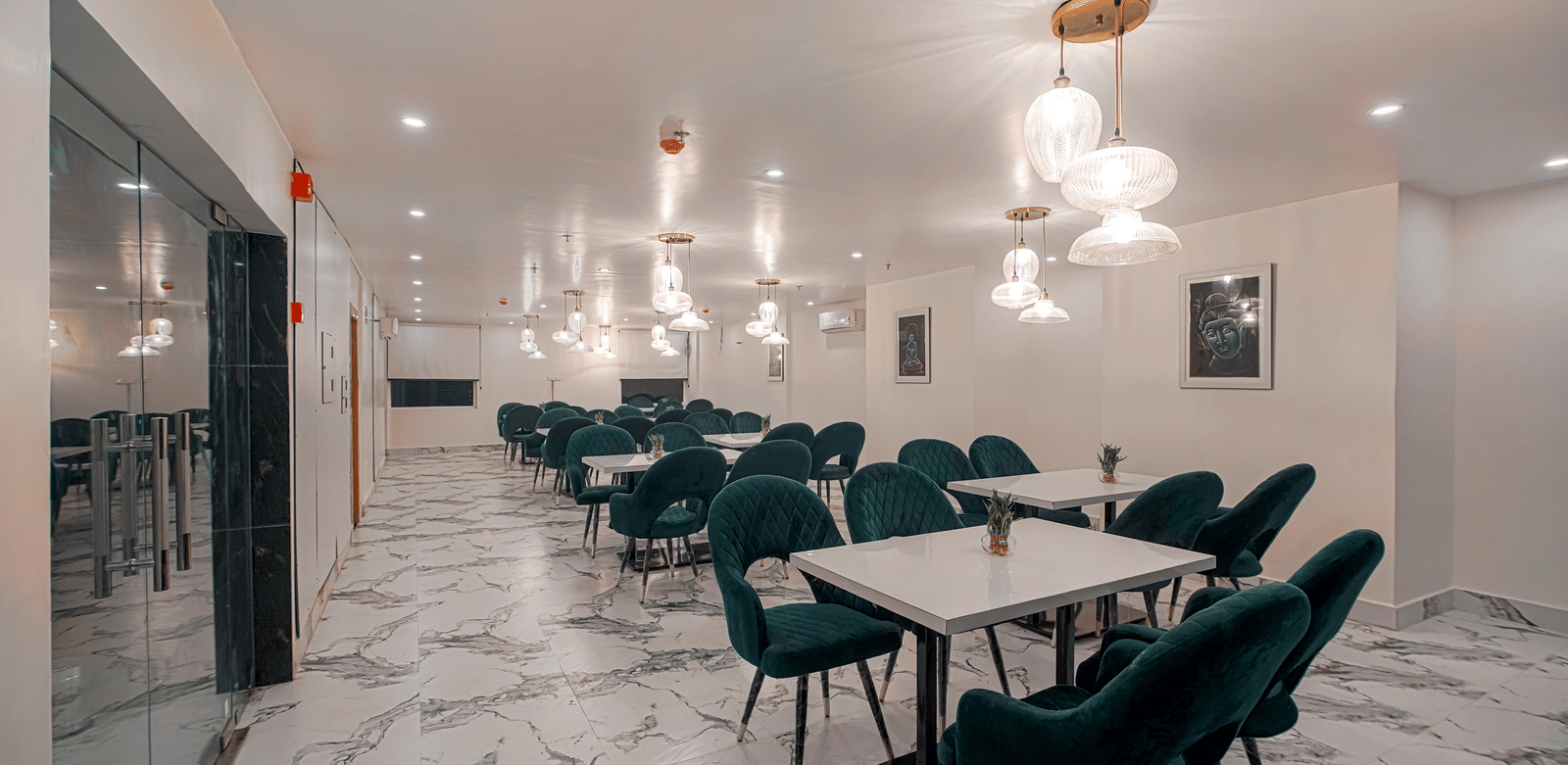 A modern white dining hall featuring elegant glass ceiling lights, neatly arranged tables and chairs at Perfectstayz Premium Varanasi.