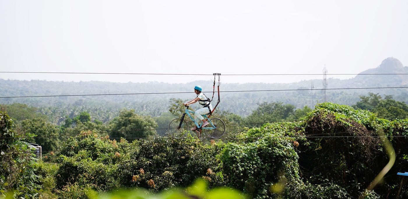 Image of a person in the air enjoying zip-cycling at Ravishing Retreat on a sunny day amid greenery