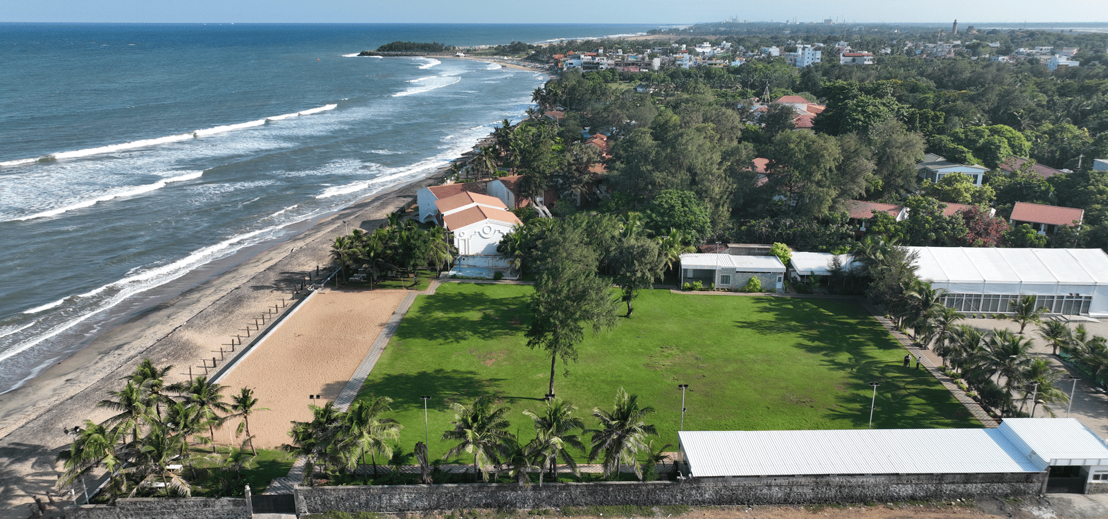 A bird’s-eye view of the sweeping coastline, where waves meet the beach sand, with Grande Bay Resort & Spa, Mamallapuram, set along the opposite side.
