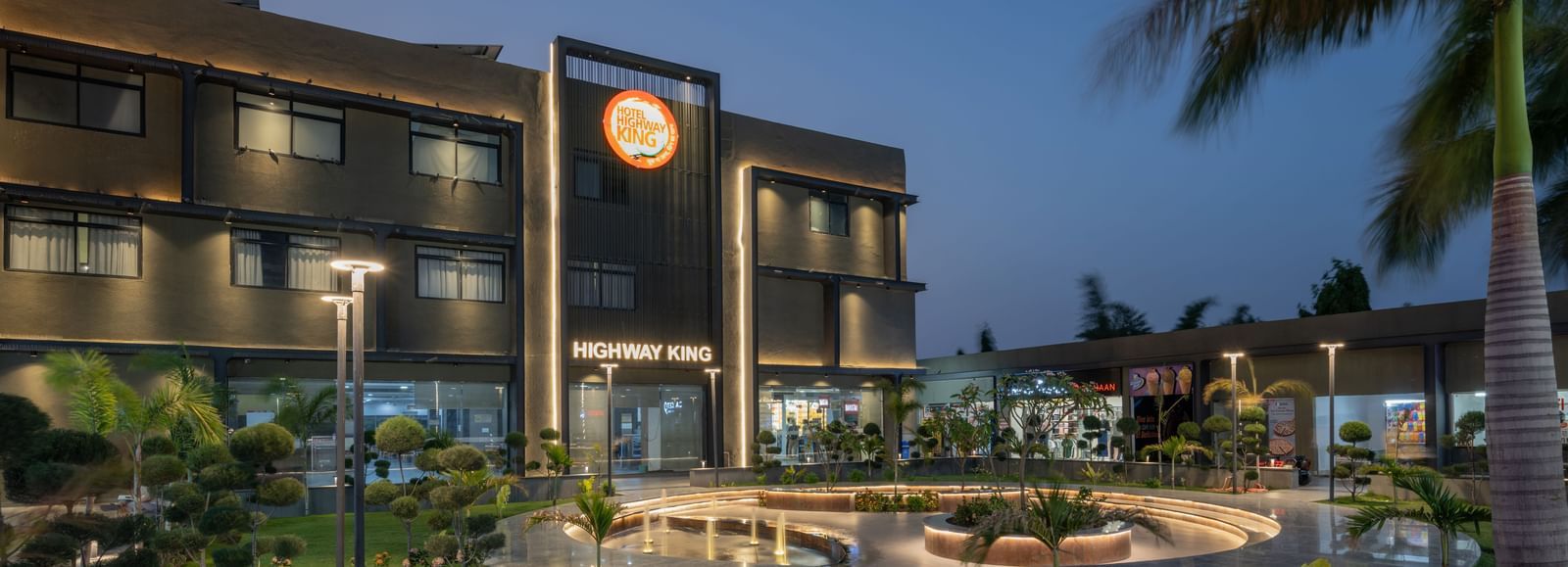 External view of Hotel Highway King, Behror featuring a well-lit facade, an illuminated logo and a well-manicured lawn.