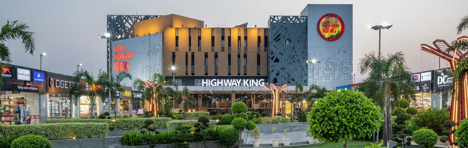 Wide-angle exterior shot of Hotel Highway King, Bilaspur, with lush landscaping and night lighting.
