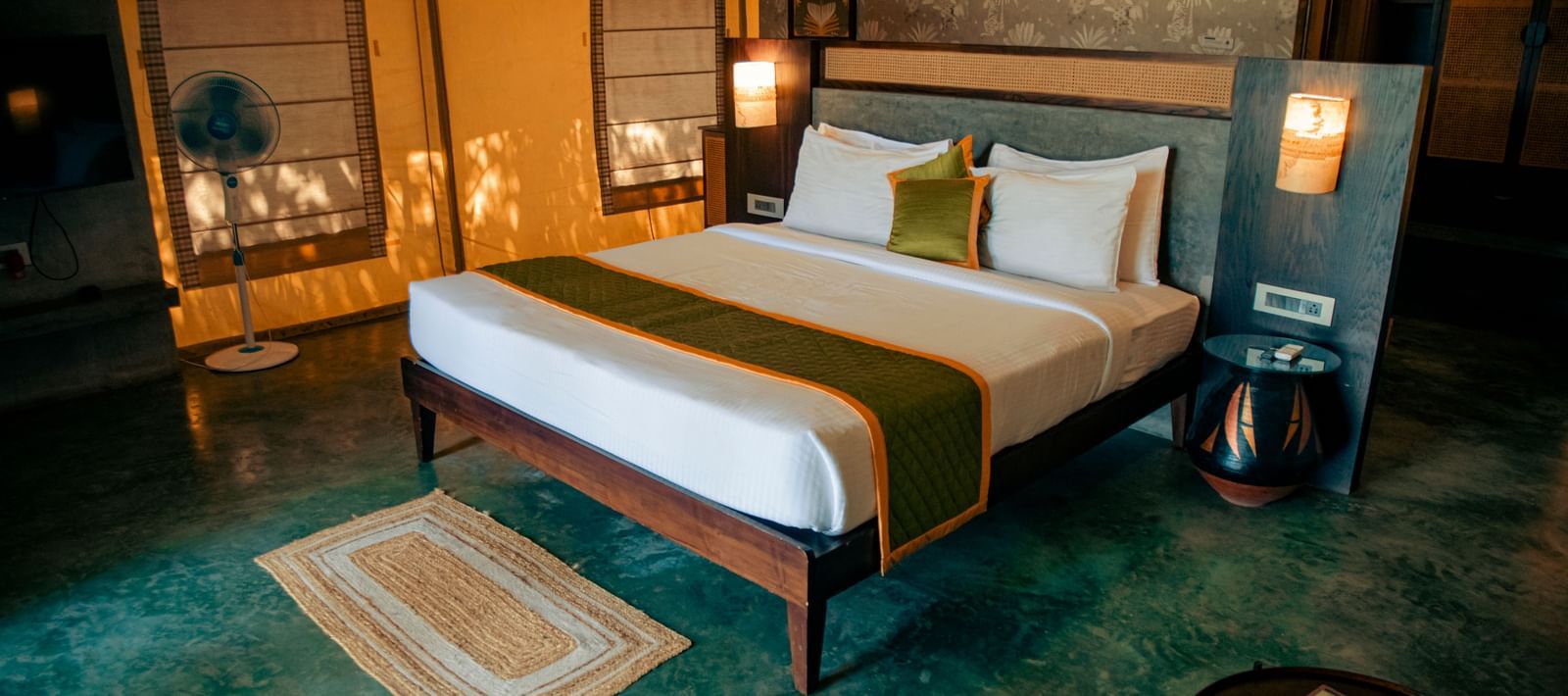 Bedroom with green flooring, king size bed, bedside lamps, and rug at Fireflies Resorts, Kabini.