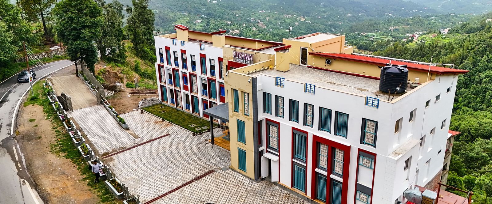 An aerial shot captures a cluster of buildings with distinct architecture amidst a sprawling green landscape | Sukama Resort & Spa, Nainital