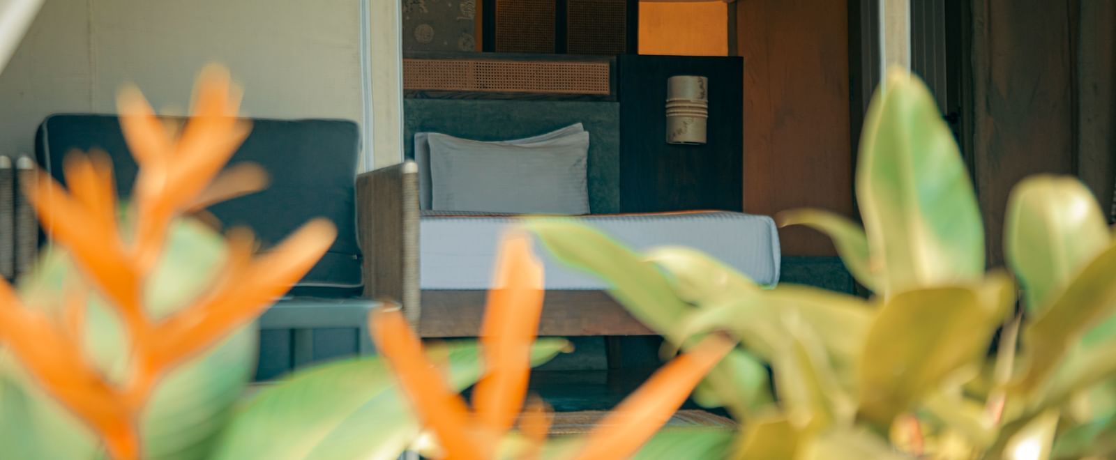 Close-up of bed with blurred orange flowers and green leaves in the foreground at Fireflies Resorts, Kabini.