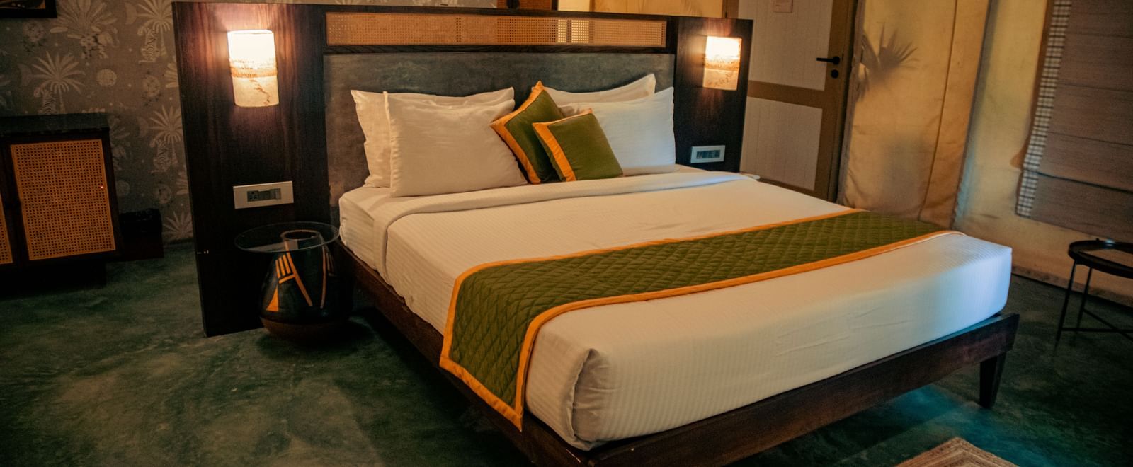 King size bed with mustard cushion, bedside lights, and green floor at Fireflies Resorts, Kabini.