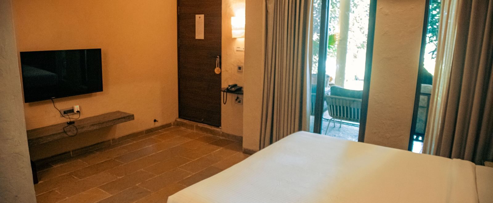 Room with a mounted TV, and a king size bed featuring glass doors leading to a balcony at Fireflies Resorts, Kabini.