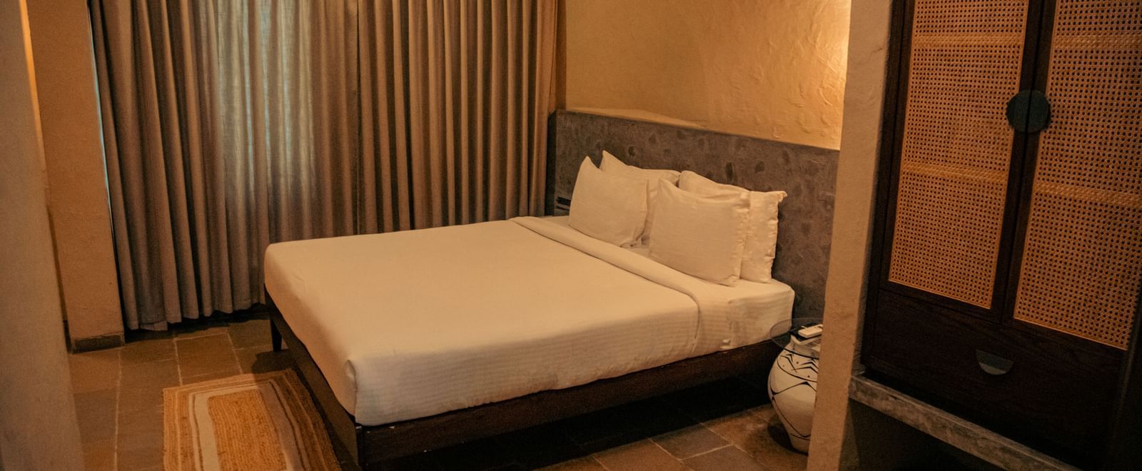 Bedroom with a king size bed, neutral furnishings, wooden flooring, and a large curtain at Fireflies Resorts, Kabini.