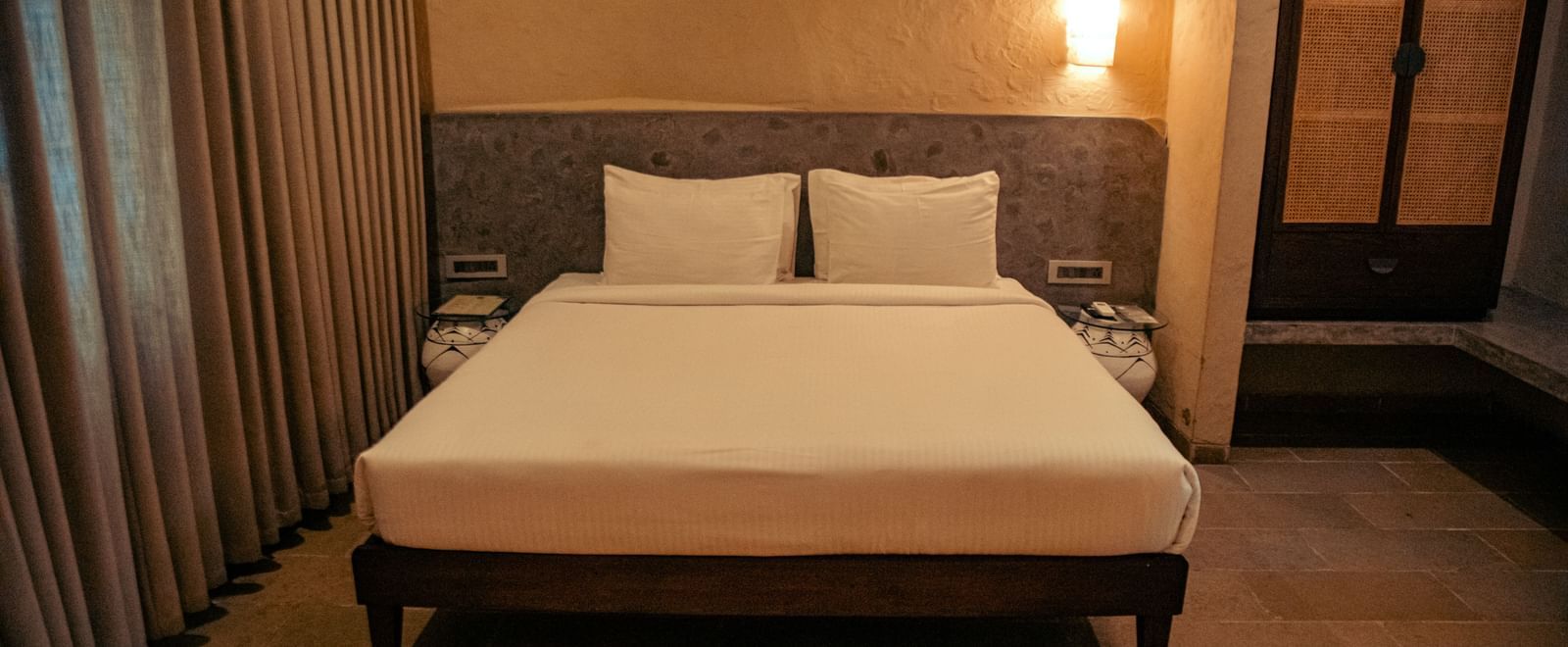 Bedroom with a king size bed, tall curtains, a wardrobe and wall-mounted lights at Fireflies Resorts, Kabini.