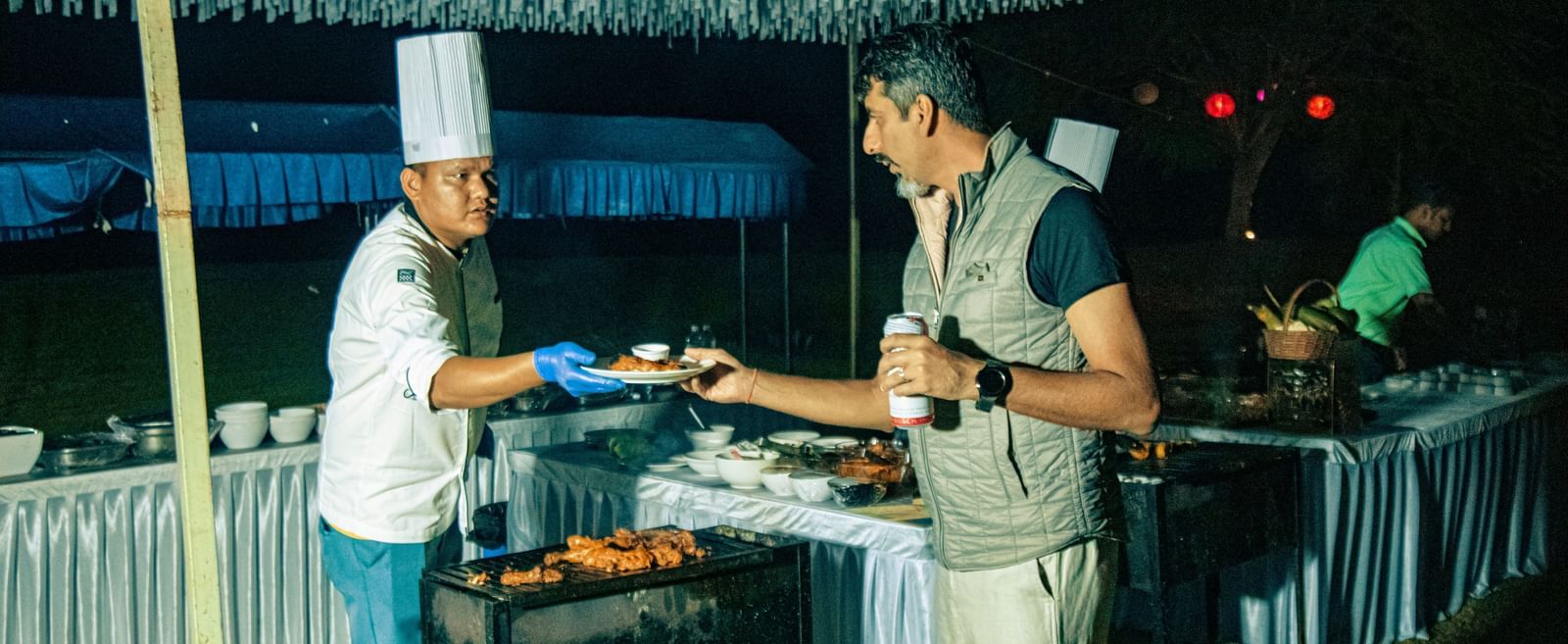 Chef serving food to a guest from a buffet counter under a canopy at Fireflies Resorts, Kabini.