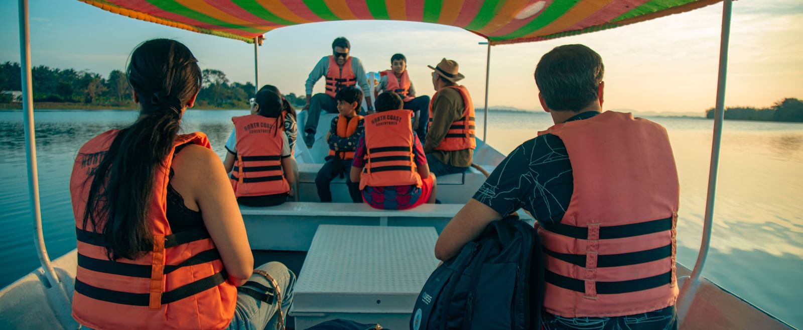 Guests wearing life jackets seated on a covered boat during a water safari at Fireflies Resorts, Kabini.