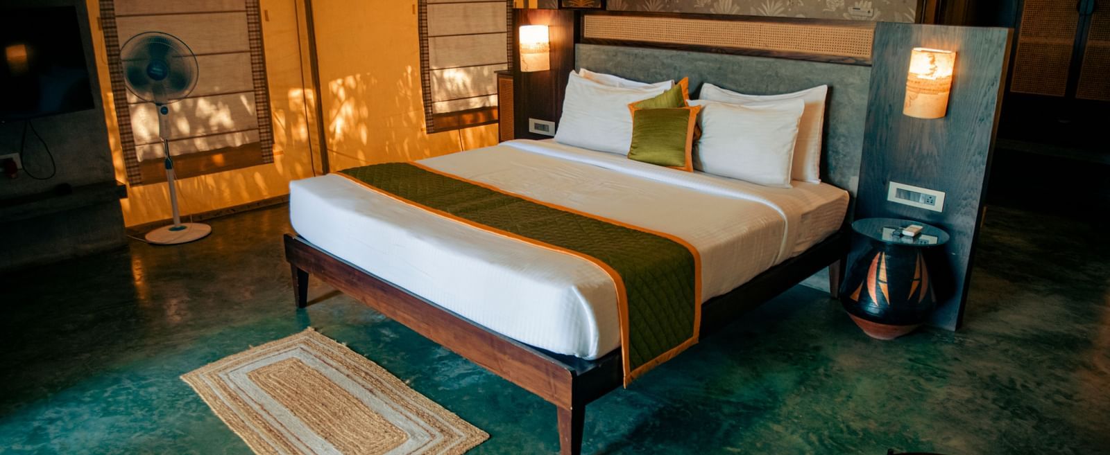 Bedroom with green flooring, king size bed, bedside lamps, and rug at Fireflies Resorts, Kabini.