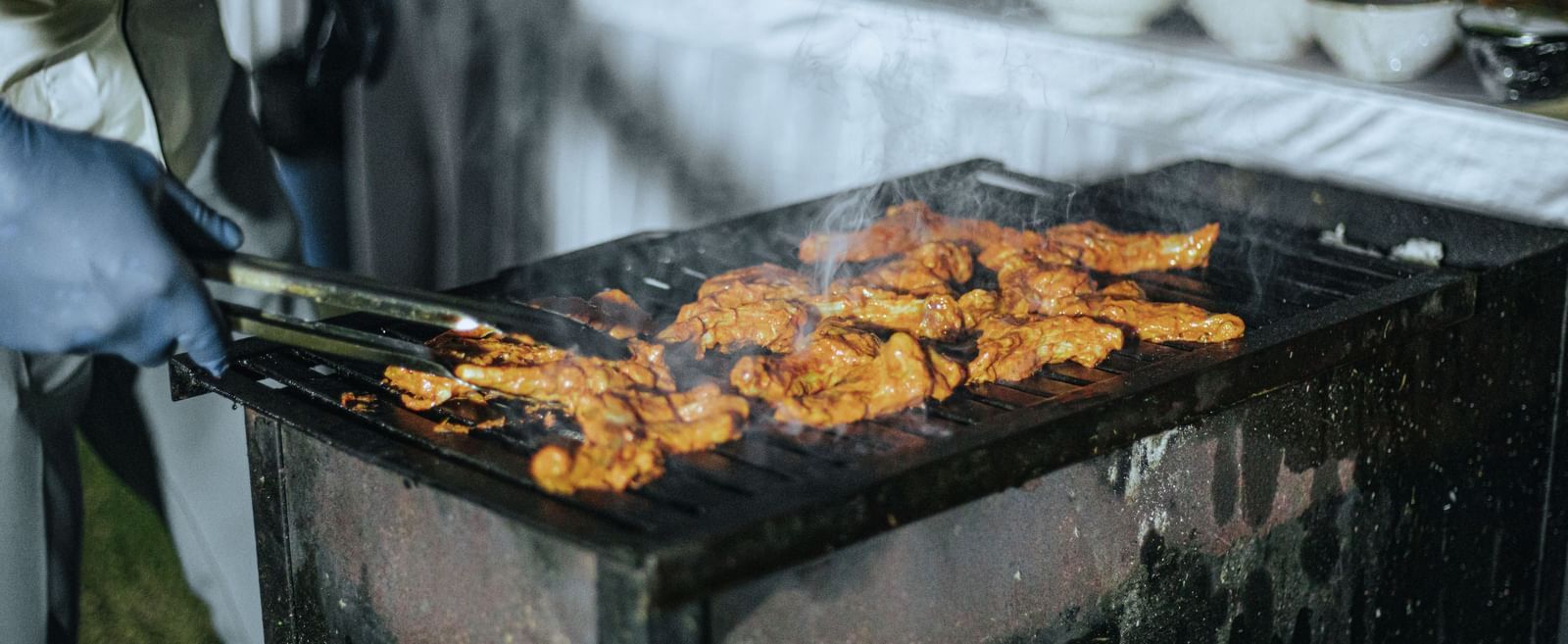 Meat skewers being grilled on an open barbecue with smoke rising at Fireflies Resorts, Kabini.