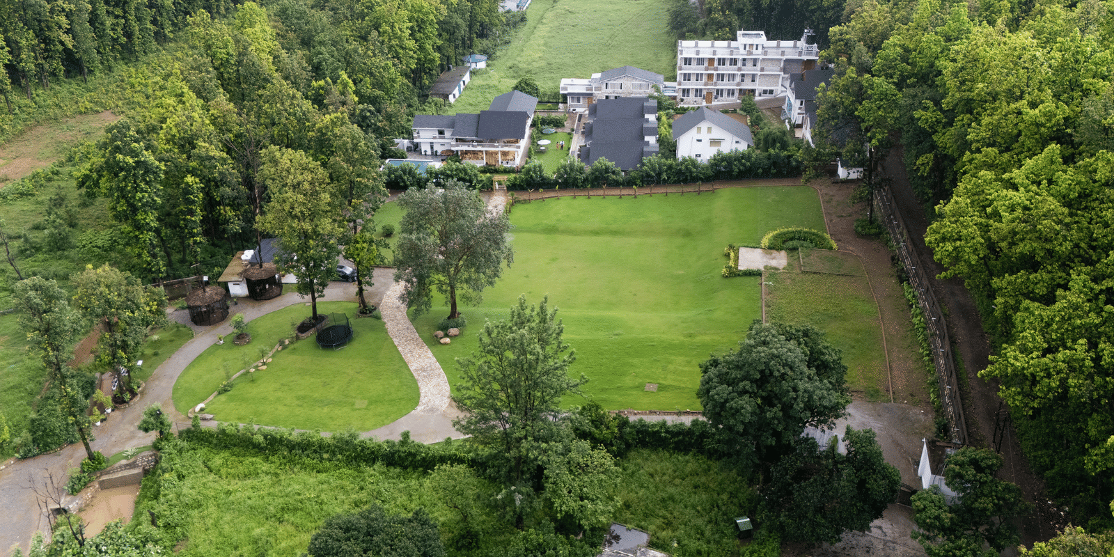 A wide view of Megha Resorts & Villas featuring the lawn, greenery and the facade.