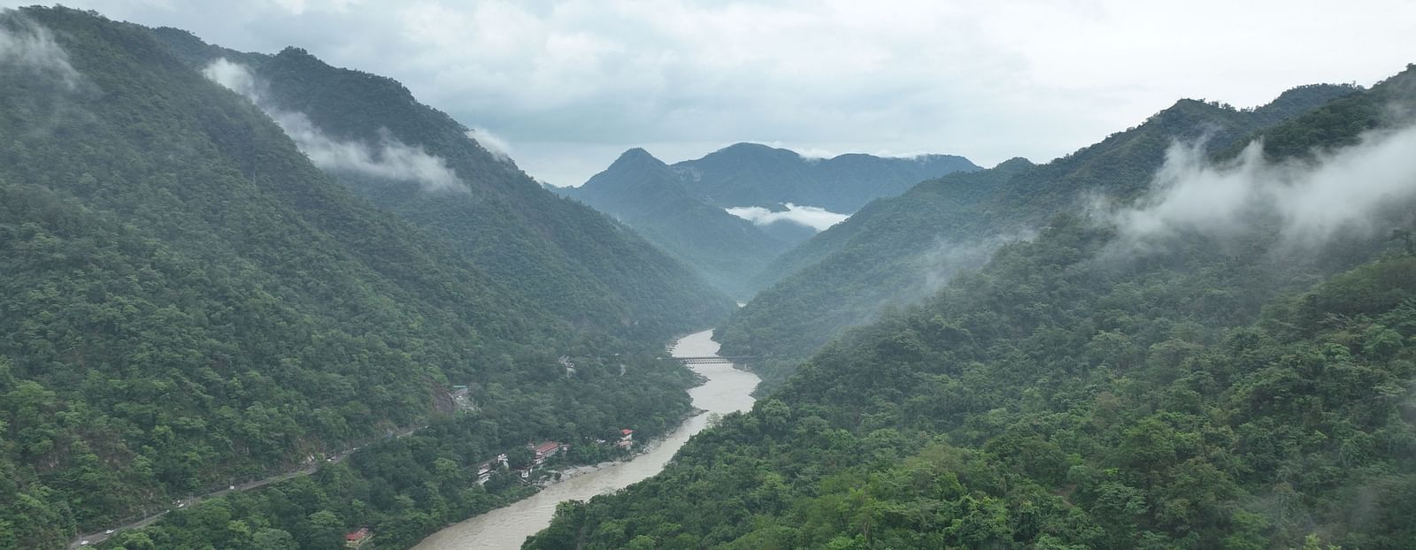A misty river winding through a lush green valley surrounded by forested mountains in Uttarakhand.