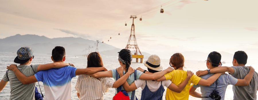 Friends sitting on a ledge near an ocean looking forward