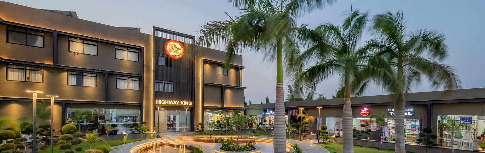 Facade and well-manicured lawn of Hotel Highway King, Behror, which also features a large illuminated logo of the property.