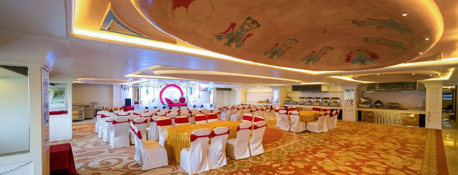 Samrat featuring a patterned carpet, round tables with chairs, and a stage area.