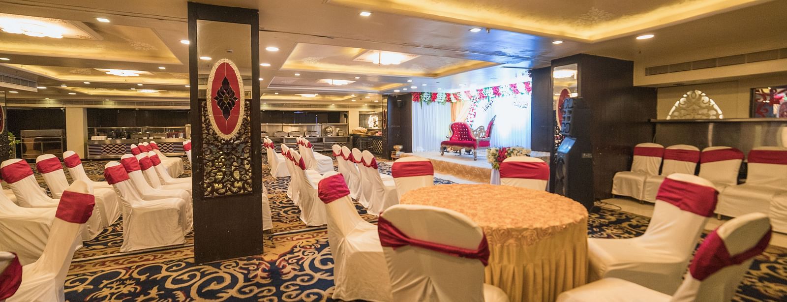 Maurya featuring round tables covered in beige cloths and white chairs, highlighting the room's carpet and pillars.