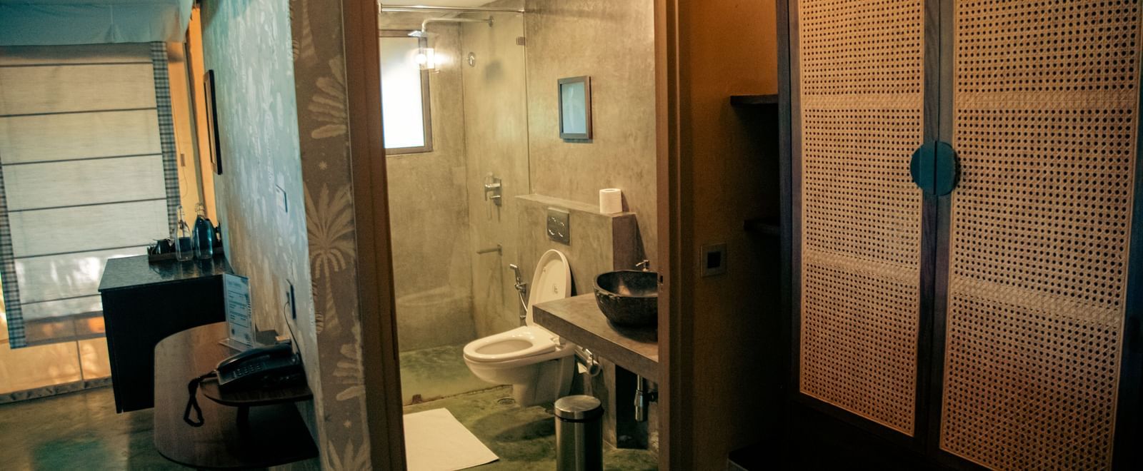 Bathroom with glass door shower area, white toilet, partially visible rack, and mirror at Fireflies Resorts, Kabini.
