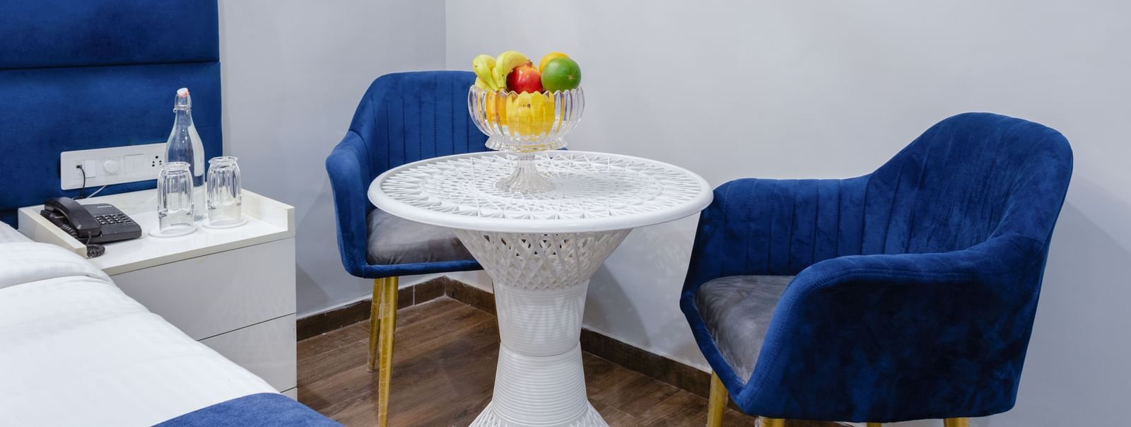 Modern seating area with blue velvet chairs and a round white table topped with fruit at Royal blue palette bedroom with king-sized bed and cosy sitting area at Hotel Downtown17, Chandigarh.