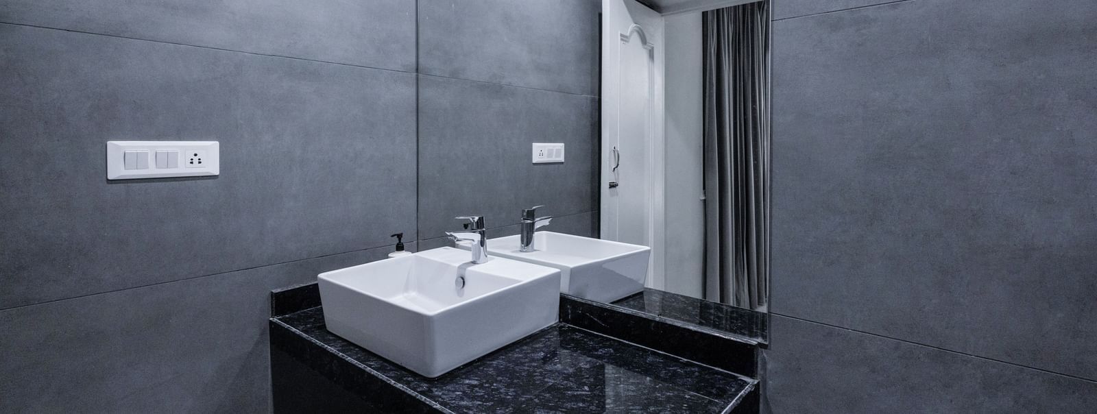 Dark-themed bathroom with rectangular sink, wall-mounted faucet, and a large mirror at Hotel Downtown17, Chandigarh.