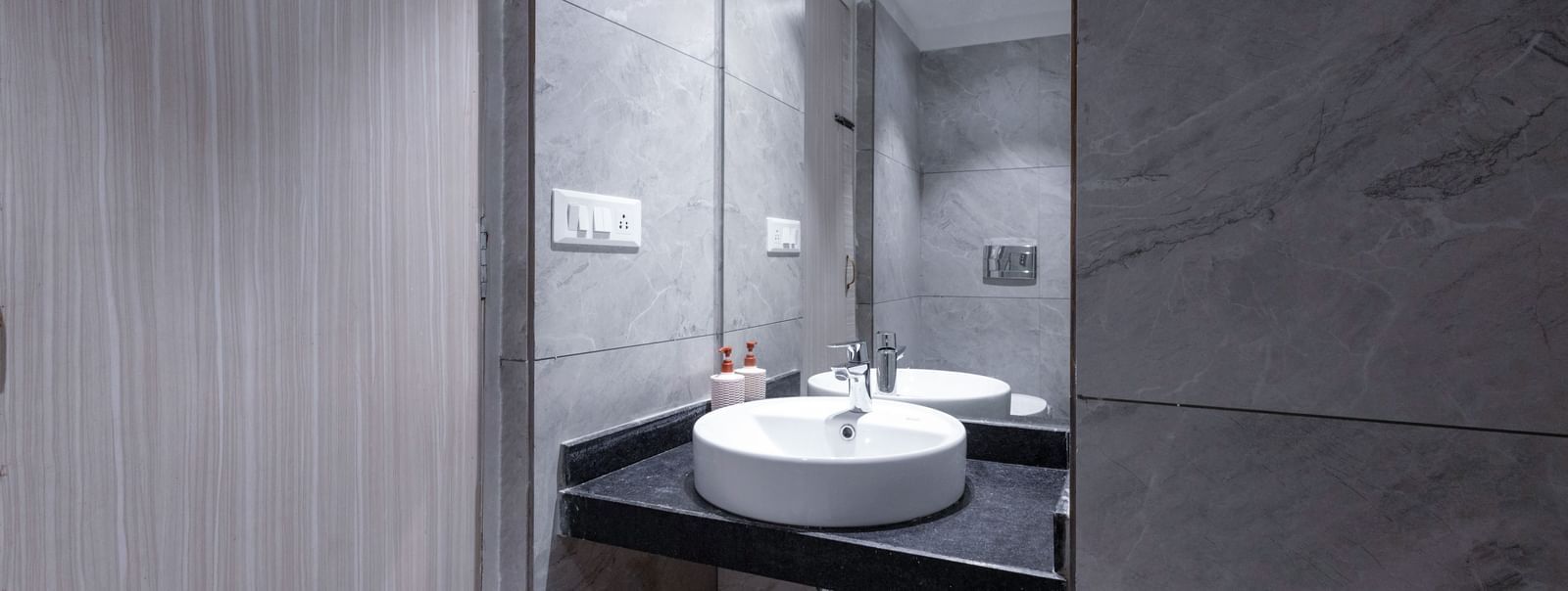Dark-toned bathroom with round sink and large mirror at Hotel Downtown17, Chandigarh.