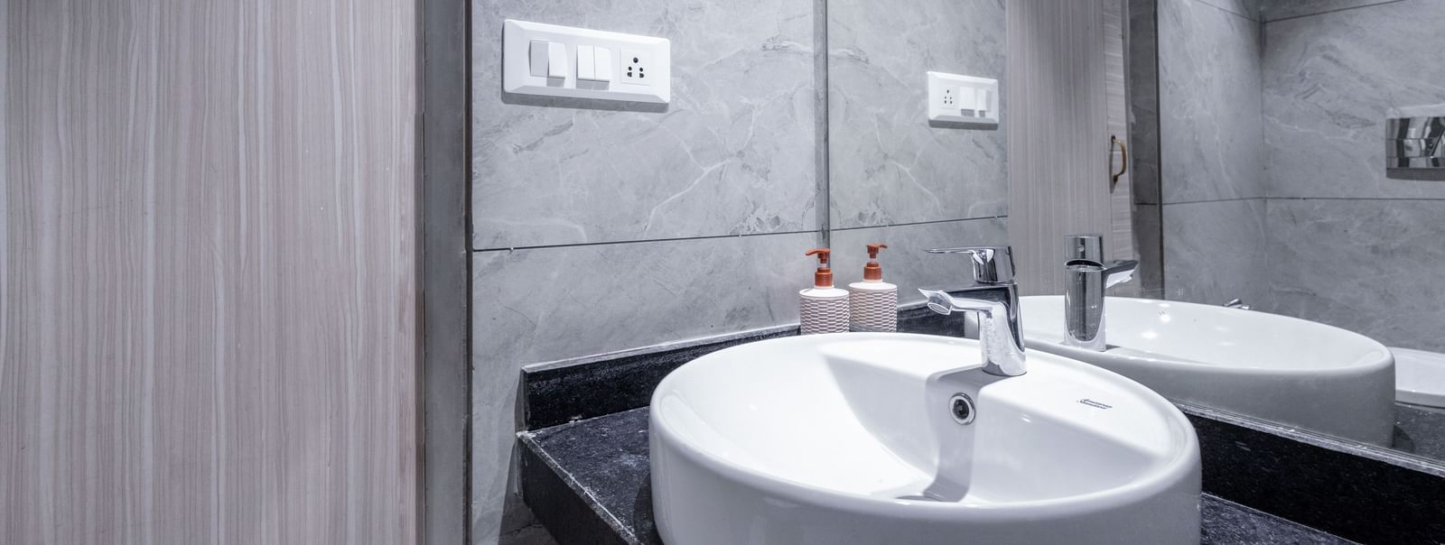 Dark-toned bathroom with round sink and large mirror at Hotel Downtown17, Chandigarh.