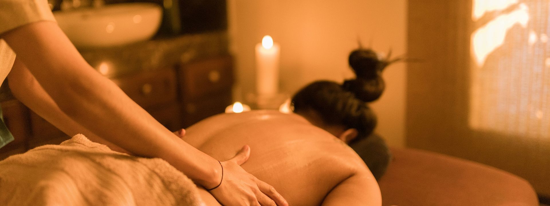 A person receiving a relaxing back massage in the warmly lit Nimoli spa with candles, soft lighting, and a calming ambience at Karma Chalets.
