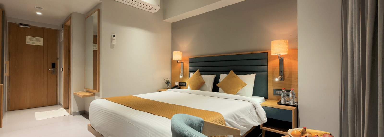 Hotel deluxe room with king size bed side tables, wall art, television, chair, desk, curtains, and window showing outdoor view