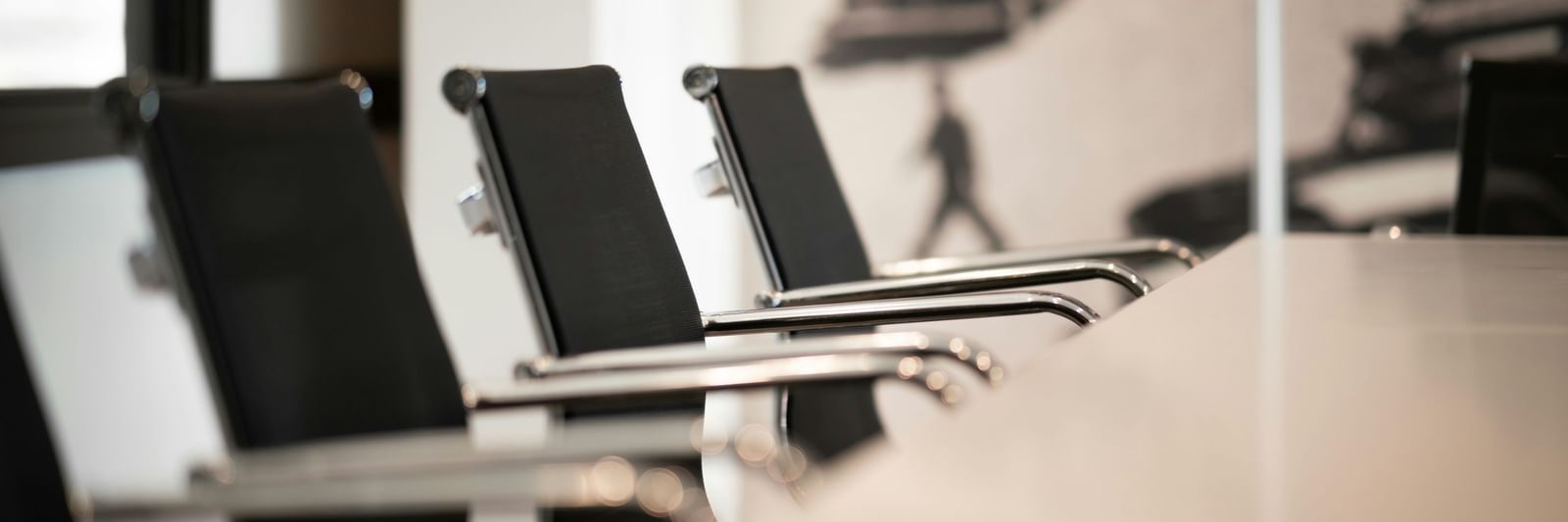 A close-up, shallow-depth-of-field shot of three modern black leather office chairs around a conference table.