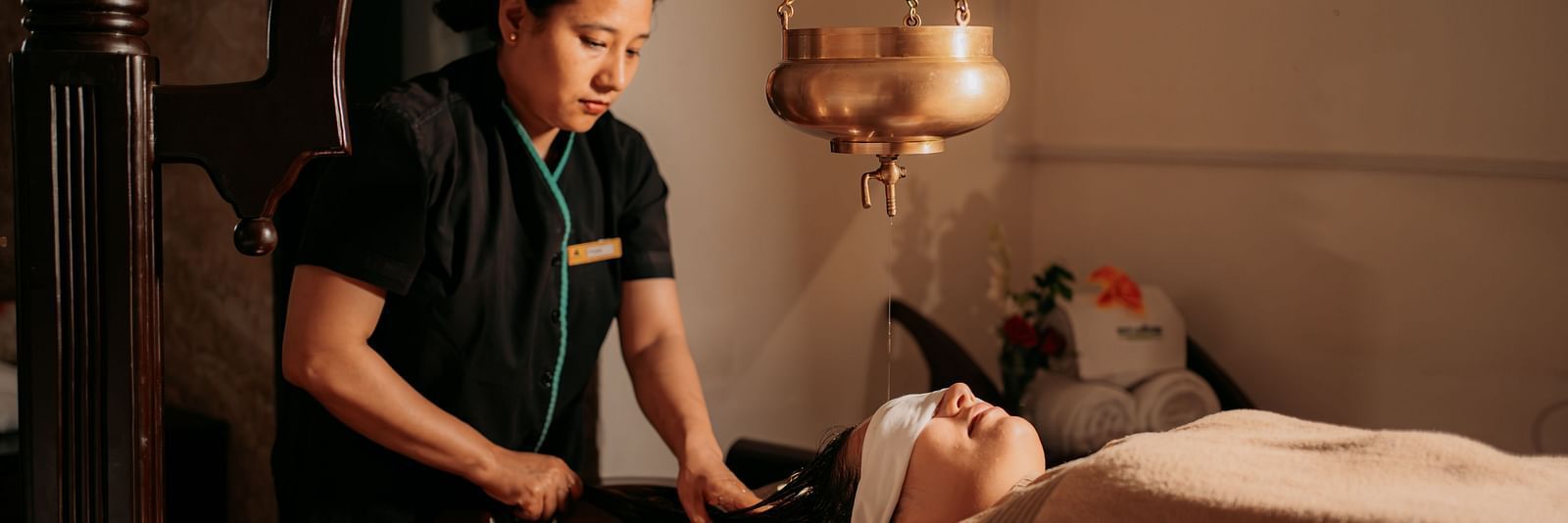 A woman offering an oil relaxation treatment to a guest reclining on the bed at Crescent spa & resort, Indore