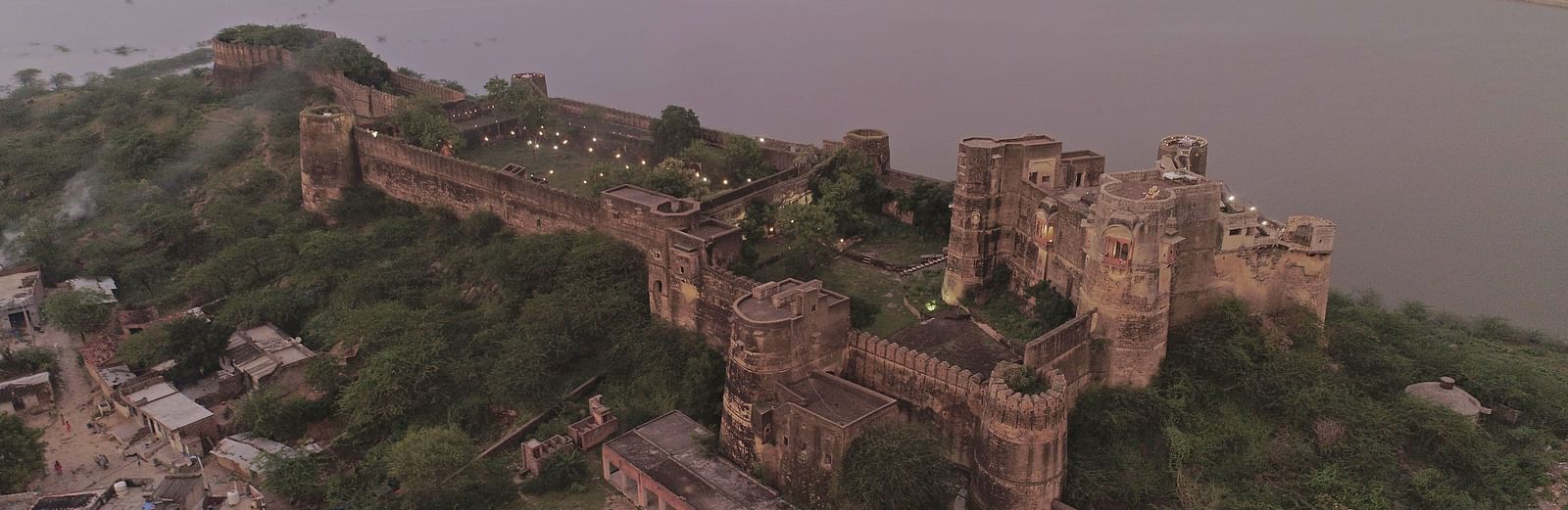 An aerial view of a ruined stone fortress perched on a hill overlooking a large body of water- Shahpura Bagh.