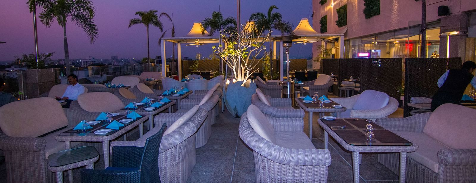 An outdoor dining setup at Hotel Ashok Nagpur with white cushioned chairs and small tables arranged for guests.