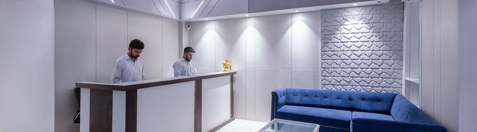 full view shot of the reception area featuring a plus blue couch along with a glass top centre table in front of it - Hotel Downtown17 Chandigarh