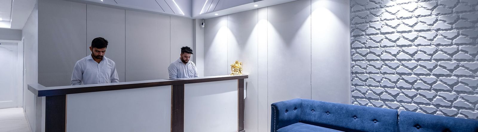 the reception area with two staff members dressed in white formal shirts standing behind the reception desk - Hotel Downtown17, Chandigarh