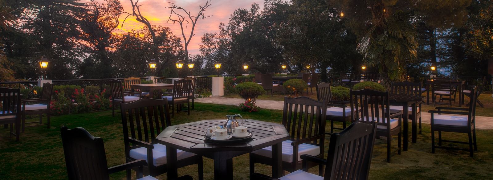 outdoor dining area with tables and chairs with the backdrop of a sunset at the Claridges Nabha Residence, Mussoorie