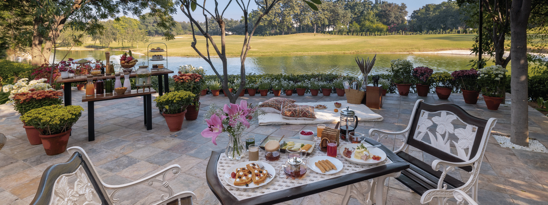 An outdoor dining setup with a table arranged with food and seating, overlooking an open green field at Karma Chalets.