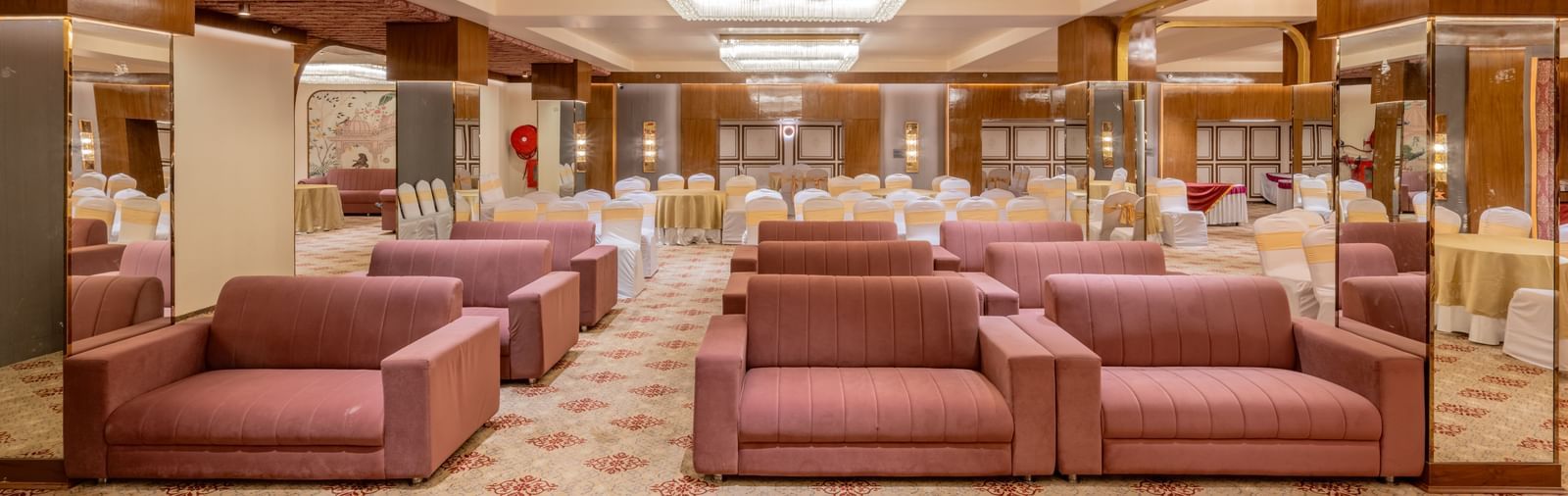 Maroon sofas arranged in a banquet hall with bright ceiling lights above at Hotel Highway King, Jaipur.