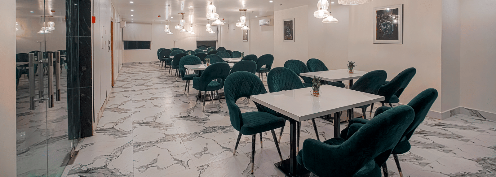 A modern white dining hall featuring elegant glass ceiling lights, neatly arranged tables and chairs at Perfectstayz Premium Varanasi.