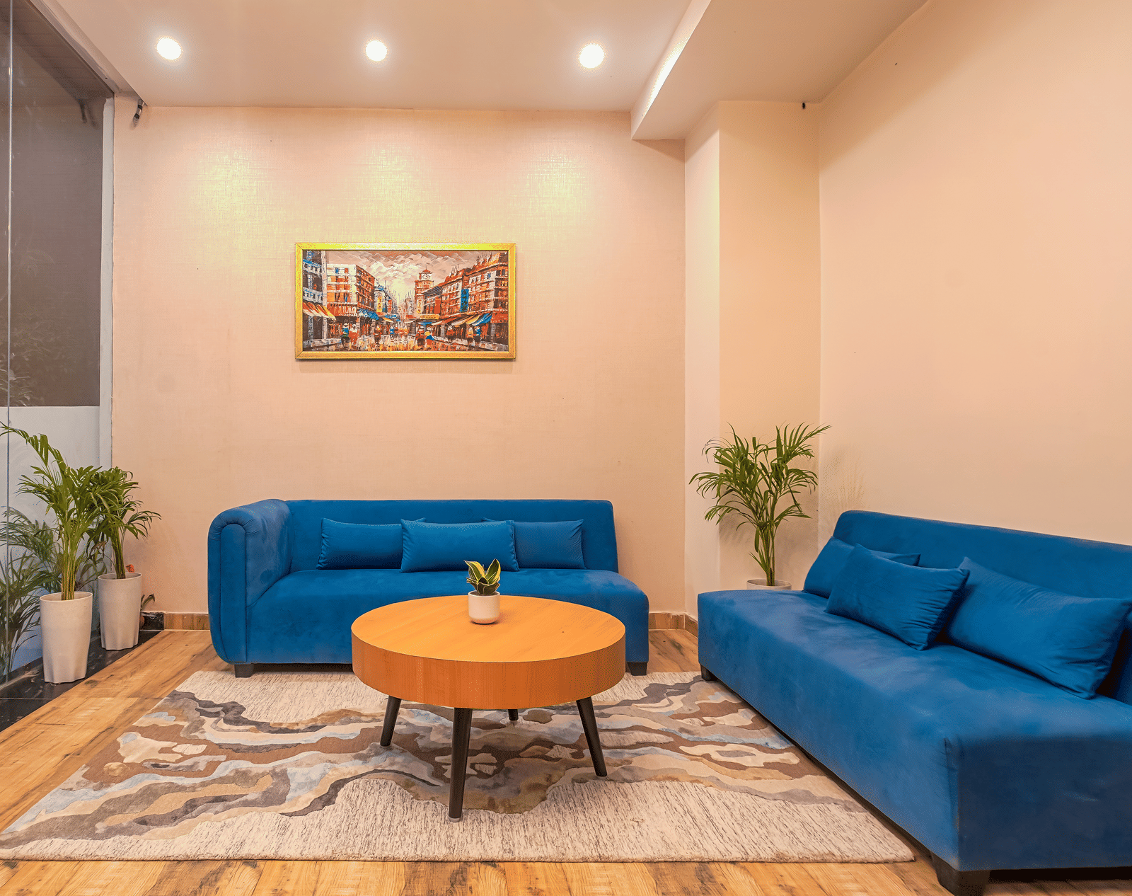 A lounge area at Perfectstayz Premium Varanasi, featuring 2 blue sofa, an artistic wall frame, a round table, and a rug.