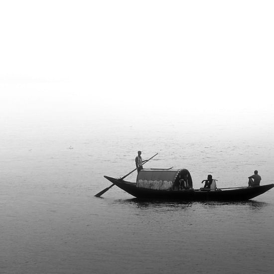 A small boat being ridden by a person with two other people on the boat in hooghly river