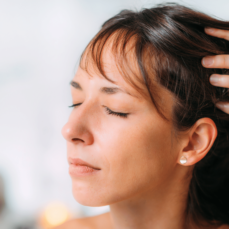 Woman receiving scalp massage with eyes closed in a spa environment.