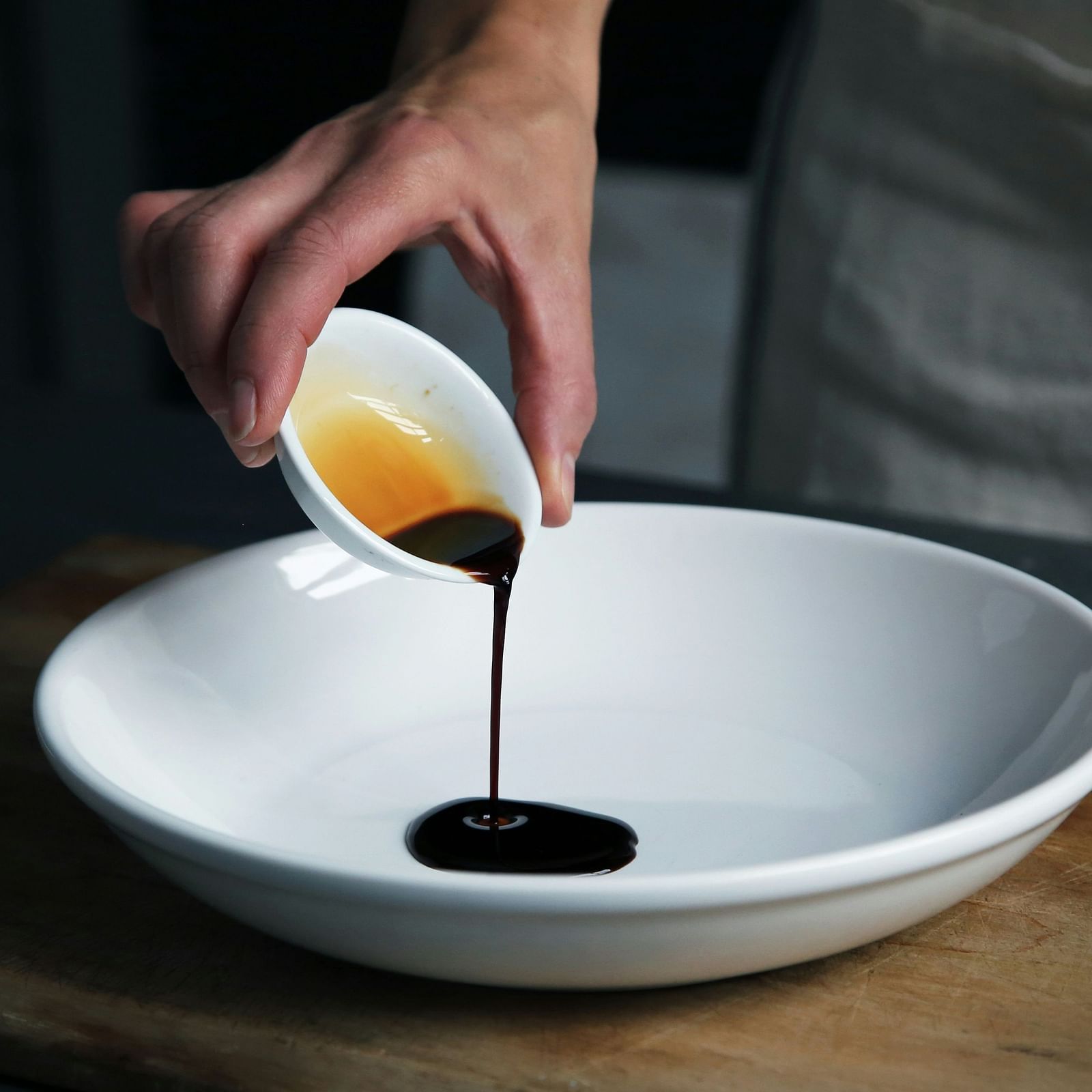 A hand pouring dark, rich Kachampuli liquid into a white bowl