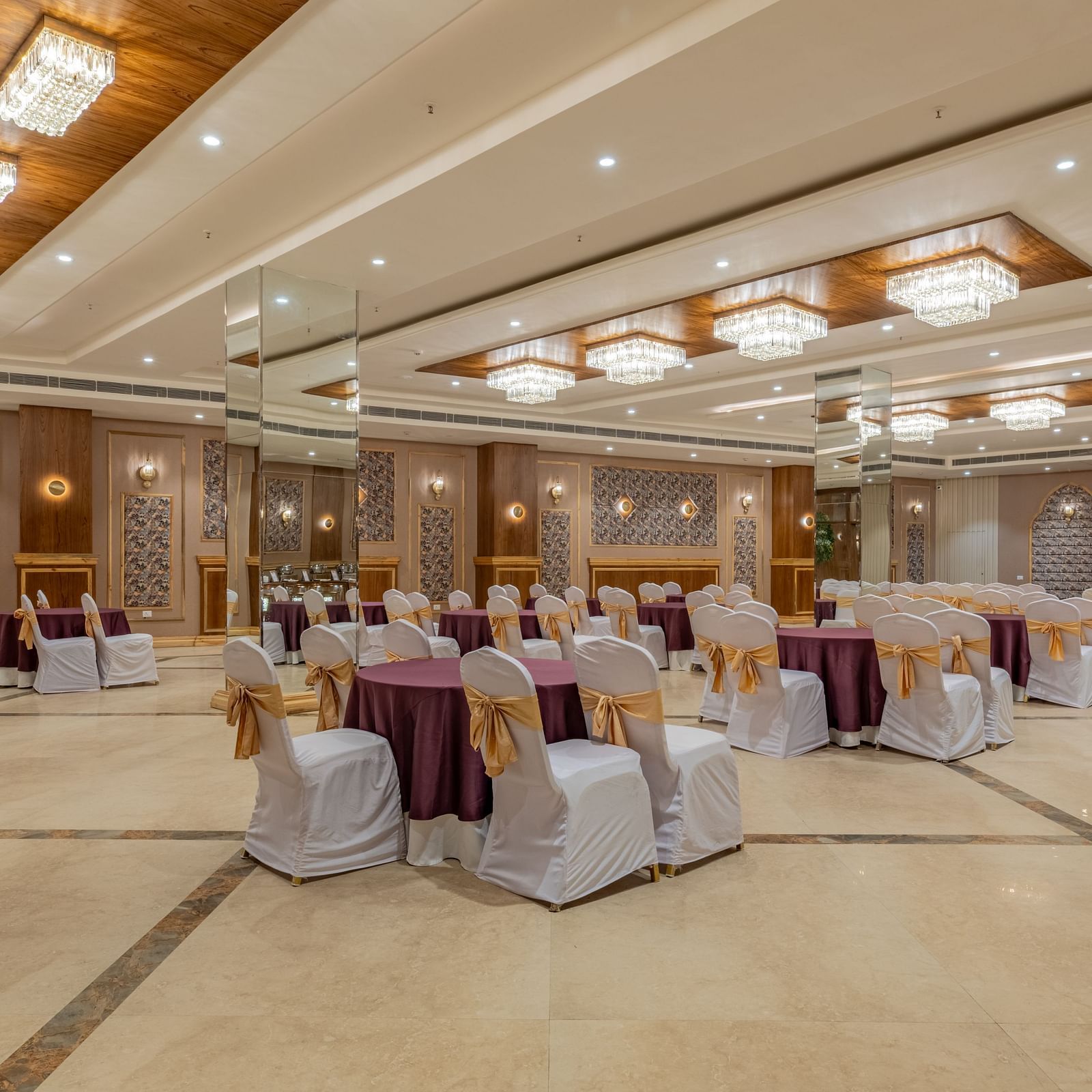 Banquet hall at Hotel Highway King, Bagru, with decorated tables and chairs, wooden accents, and elegant ceiling lighting.
