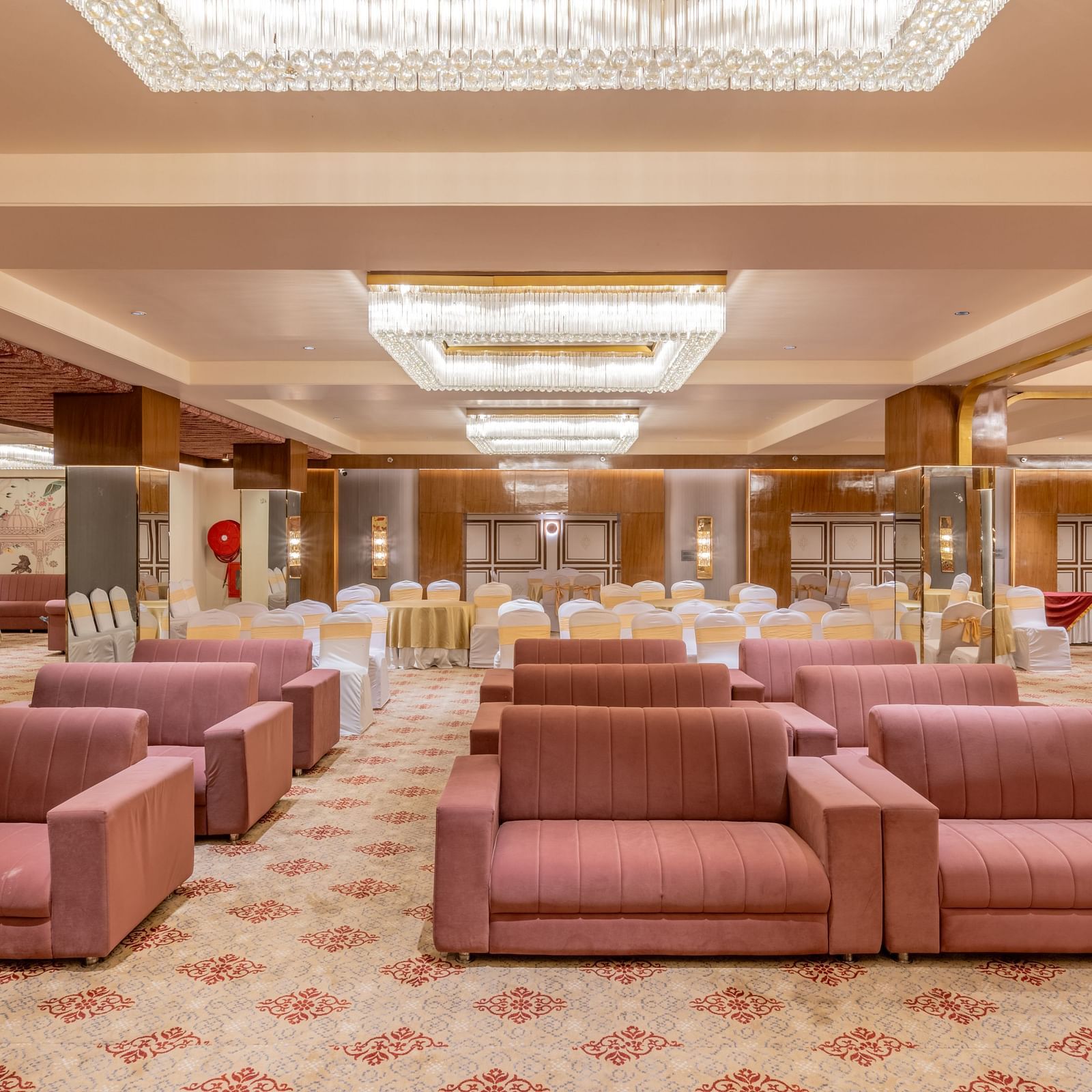 Maroon sofas arranged in a banquet hall with bright ceiling lights above at Hotel Highway King, Jaipur.