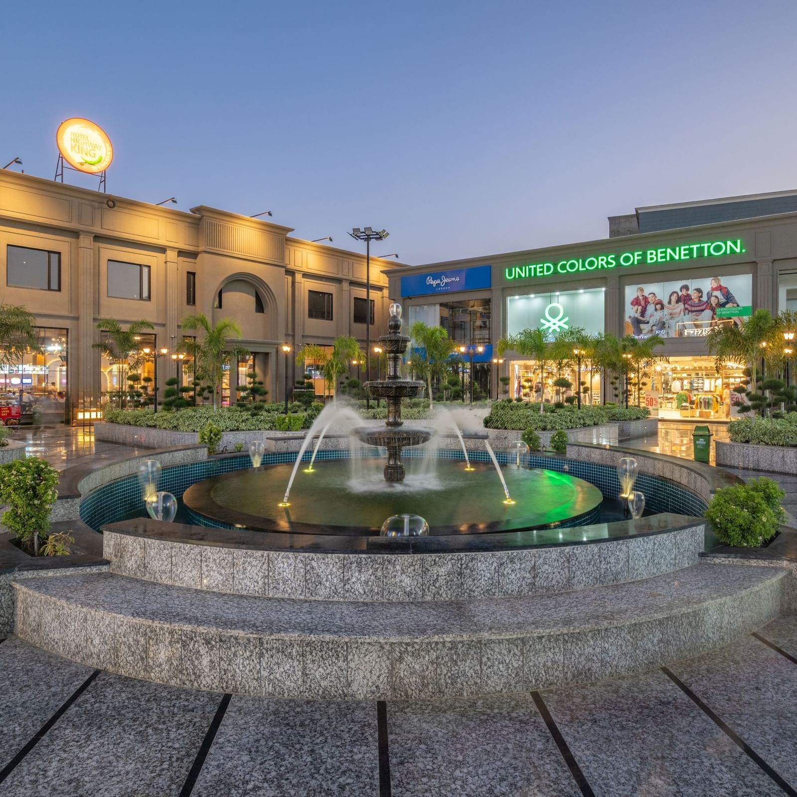 Fountain courtyard with landscaped area and building view at Hotel Highway King, Kishangarh during evening.