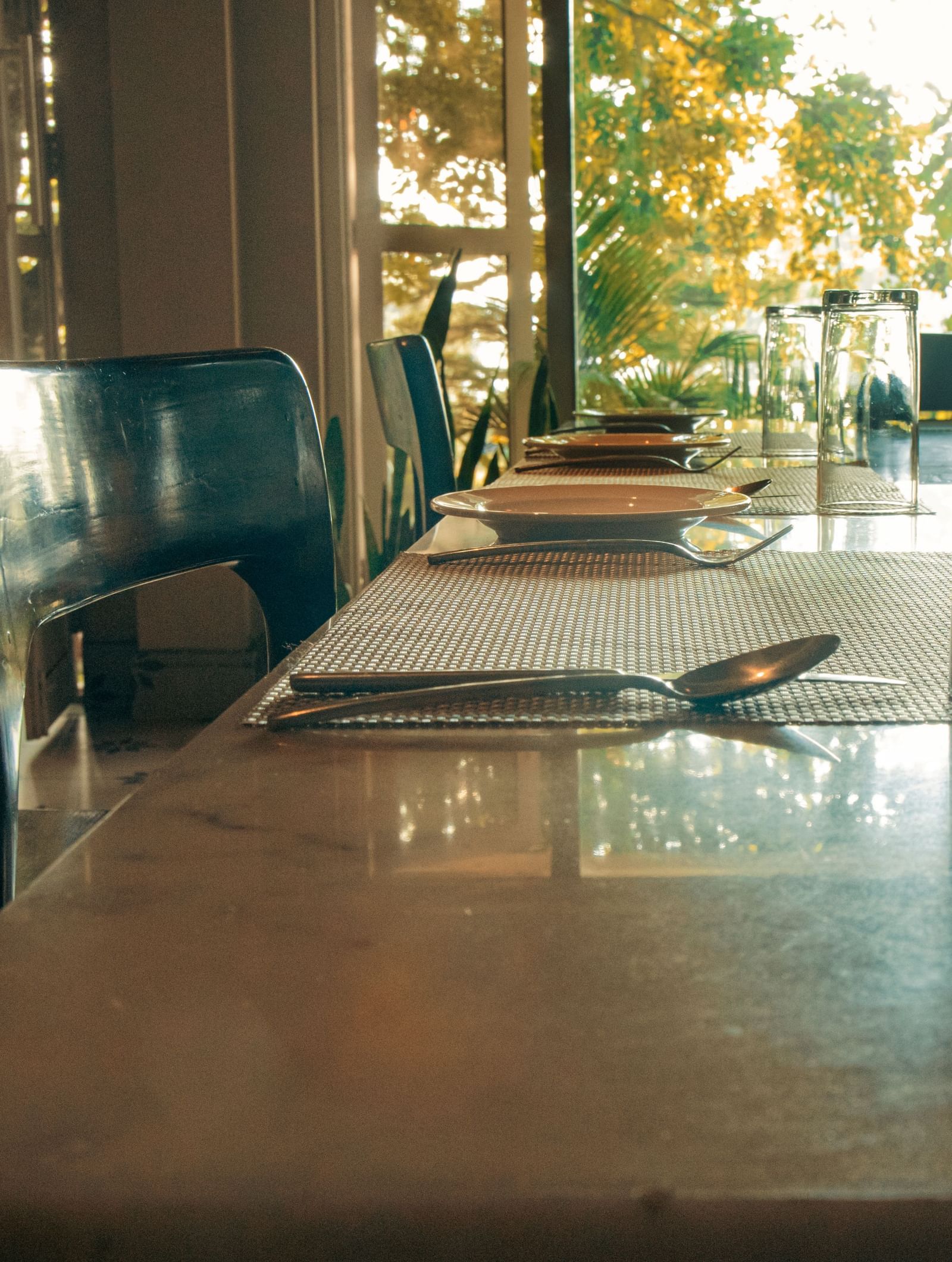 Indoor dining area with wooden tables, cushioned chairs, and sunlight streaming through glass doors at Fireflies Resorts, Kabini.